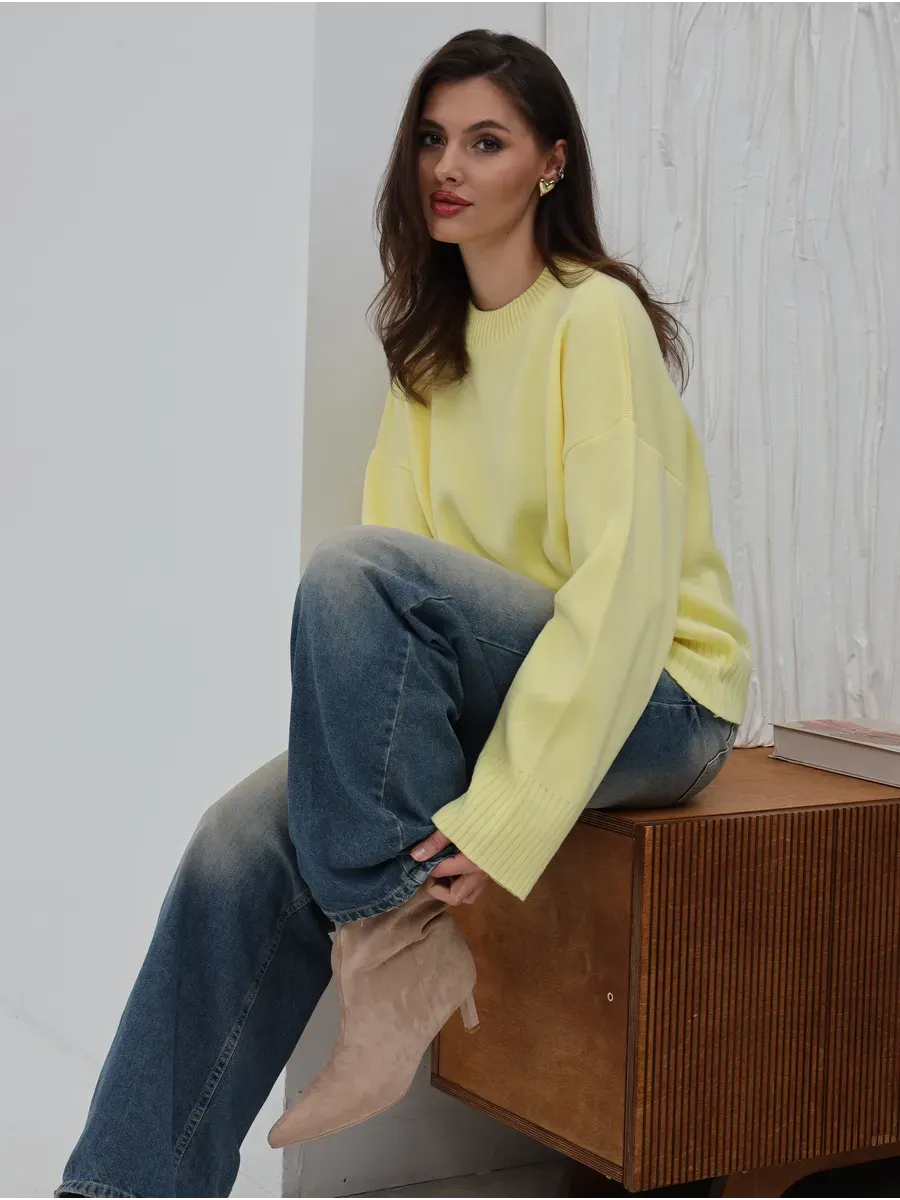 Woman wearing Solara Sweater by Lauven in light yellow, styled with blue jeans on a wooden surface.