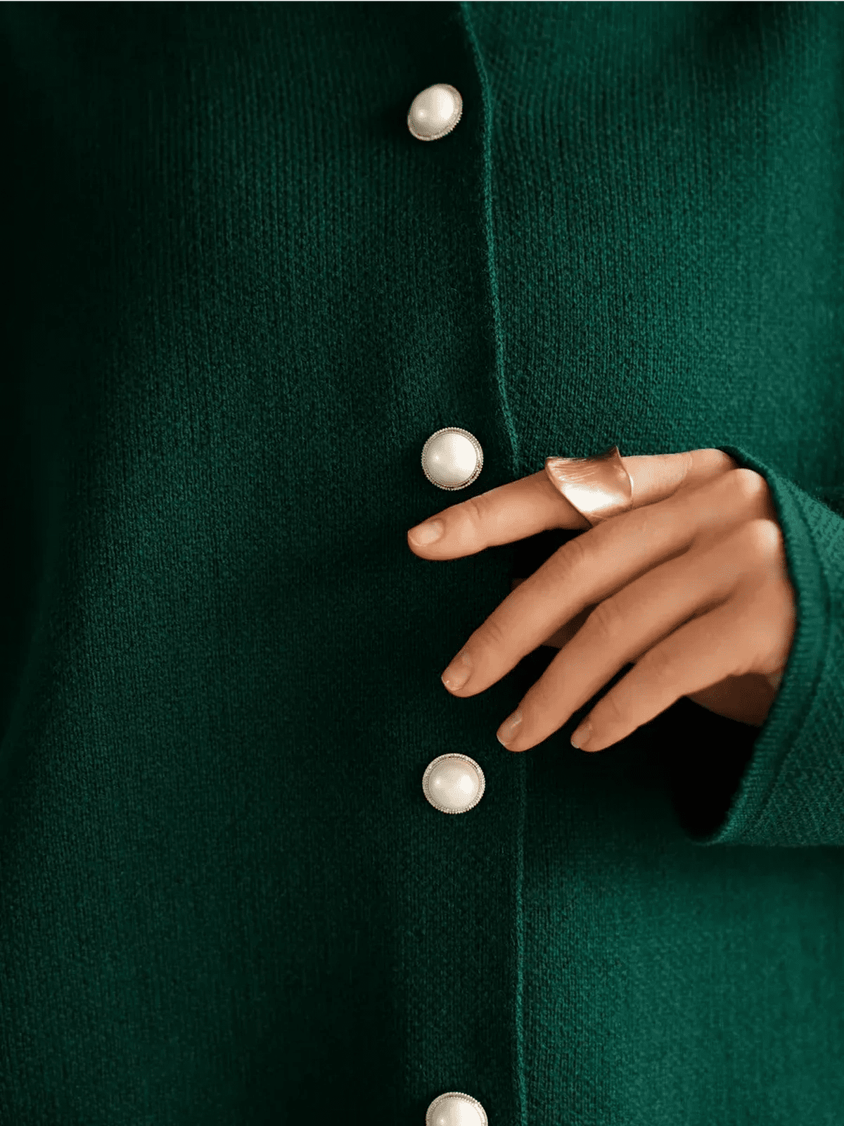 Close-up of Lauven's Verdant Cardigan, showcasing emerald knit and button closure with a hand wearing a gold ring.