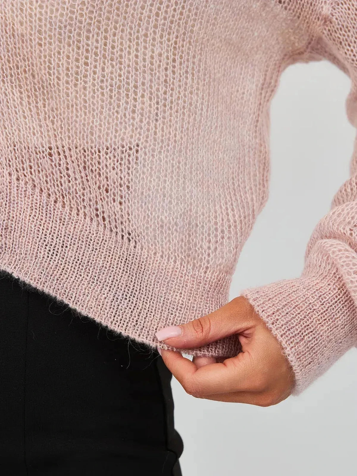 Close-up of a woman's hand holding the hem of the Rose Cardigan by Lauven, showcasing lightweight pink mohair-blend knitwear.