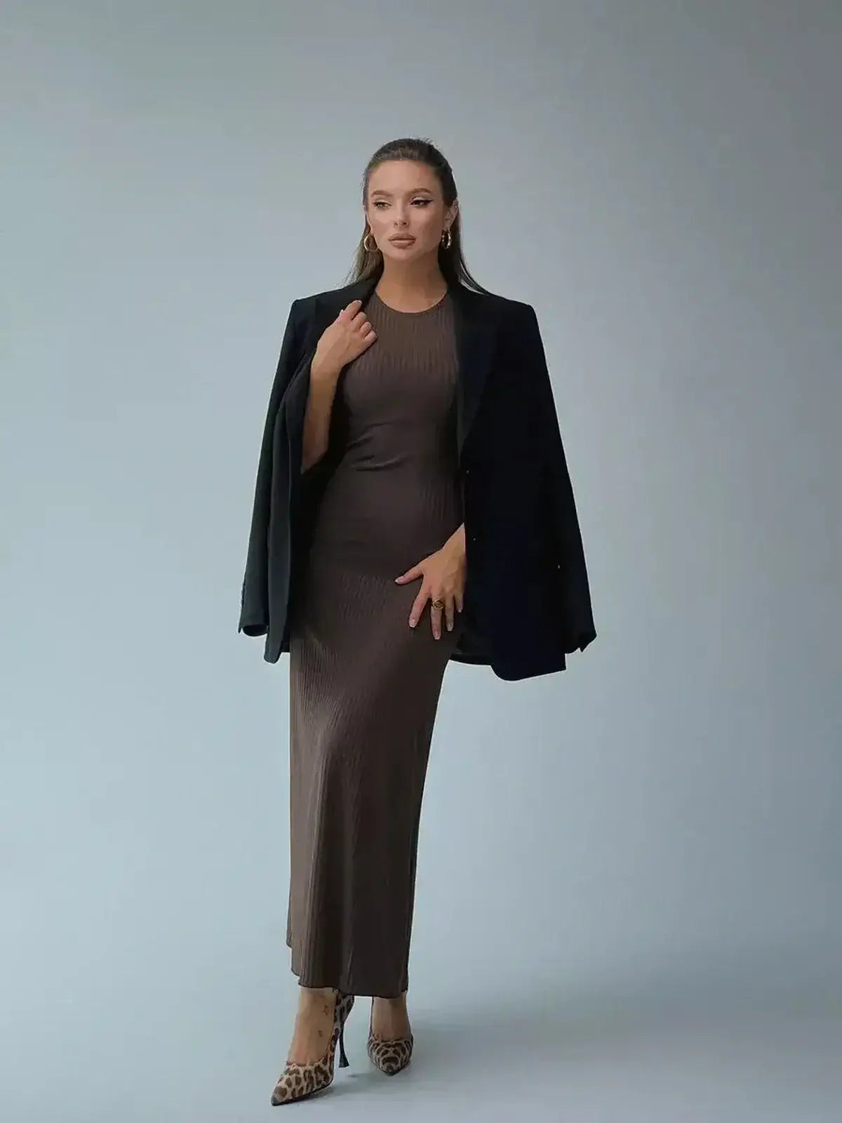 Model showcasing the Maxi Dress Sculpted Ease, a sleek ribbed knit dress, paired with a black blazer for an elegant look.