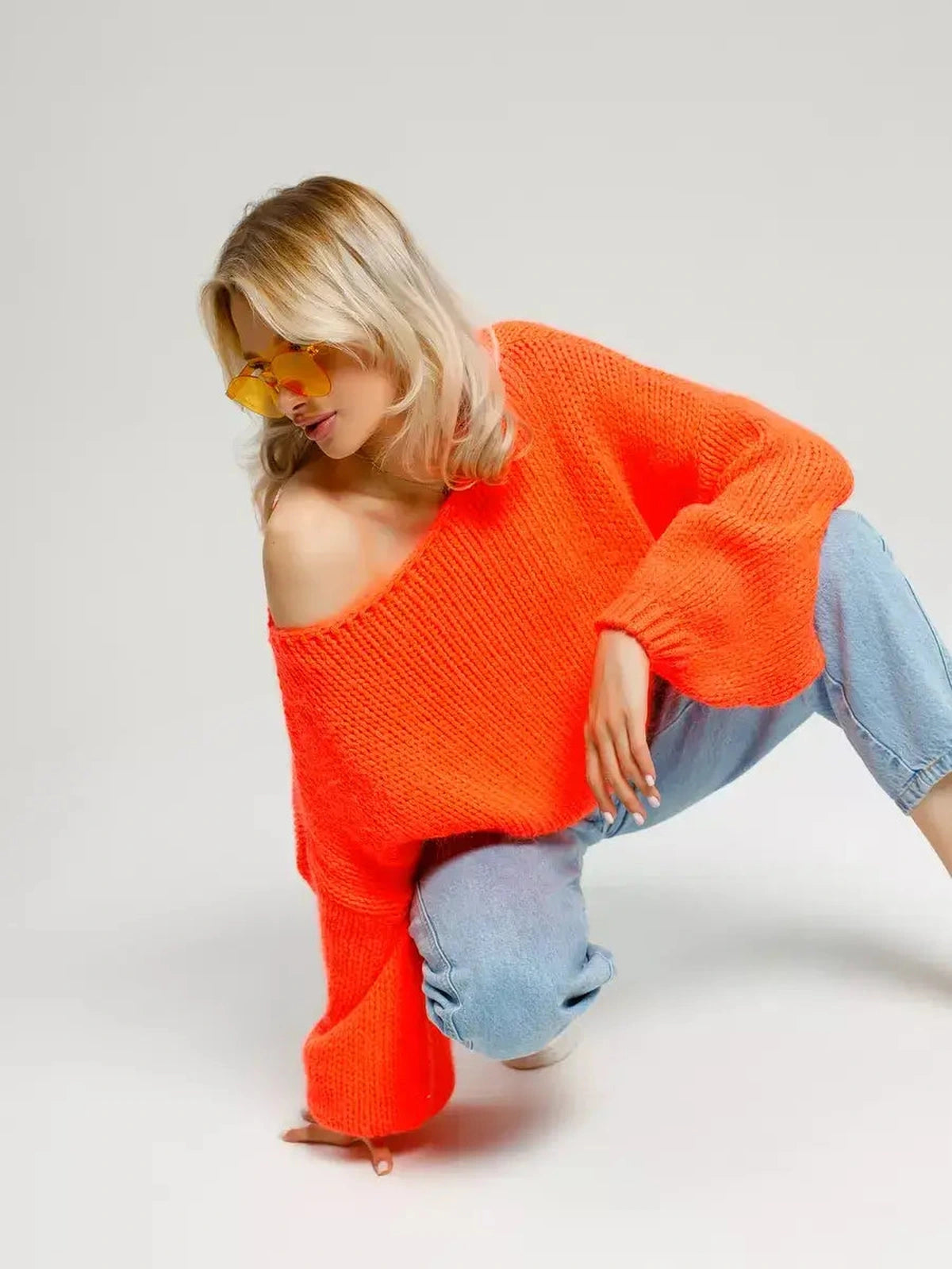 Nova Sweater by Lauven in oversized off-shoulder neon orange knit, stylishly worn with light blue jeans.