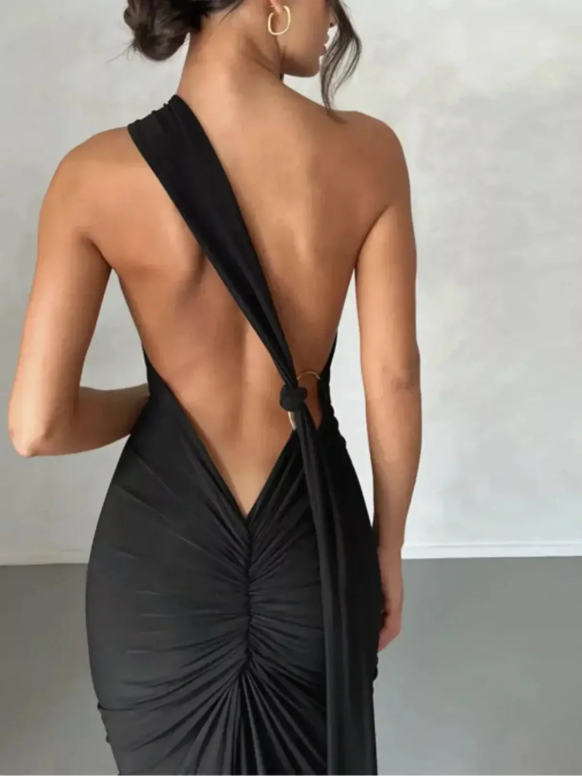 Back view of a woman in the Obsidian Maxi Dress showcasing its asymmetrical design and elegant drape.