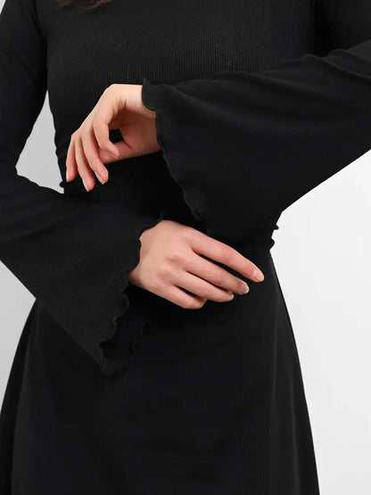 Close-up of a woman wearing a black dress with flared long sleeves, highlighting the soft ribbed fabric.