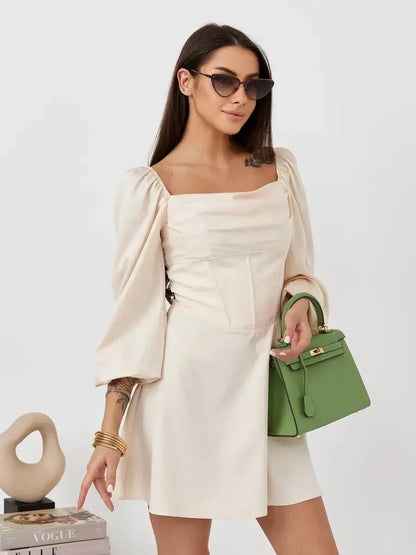 Model showcasing the Lace Muse beige mini dress with puff sleeves, styled with a green handbag and sunglasses.