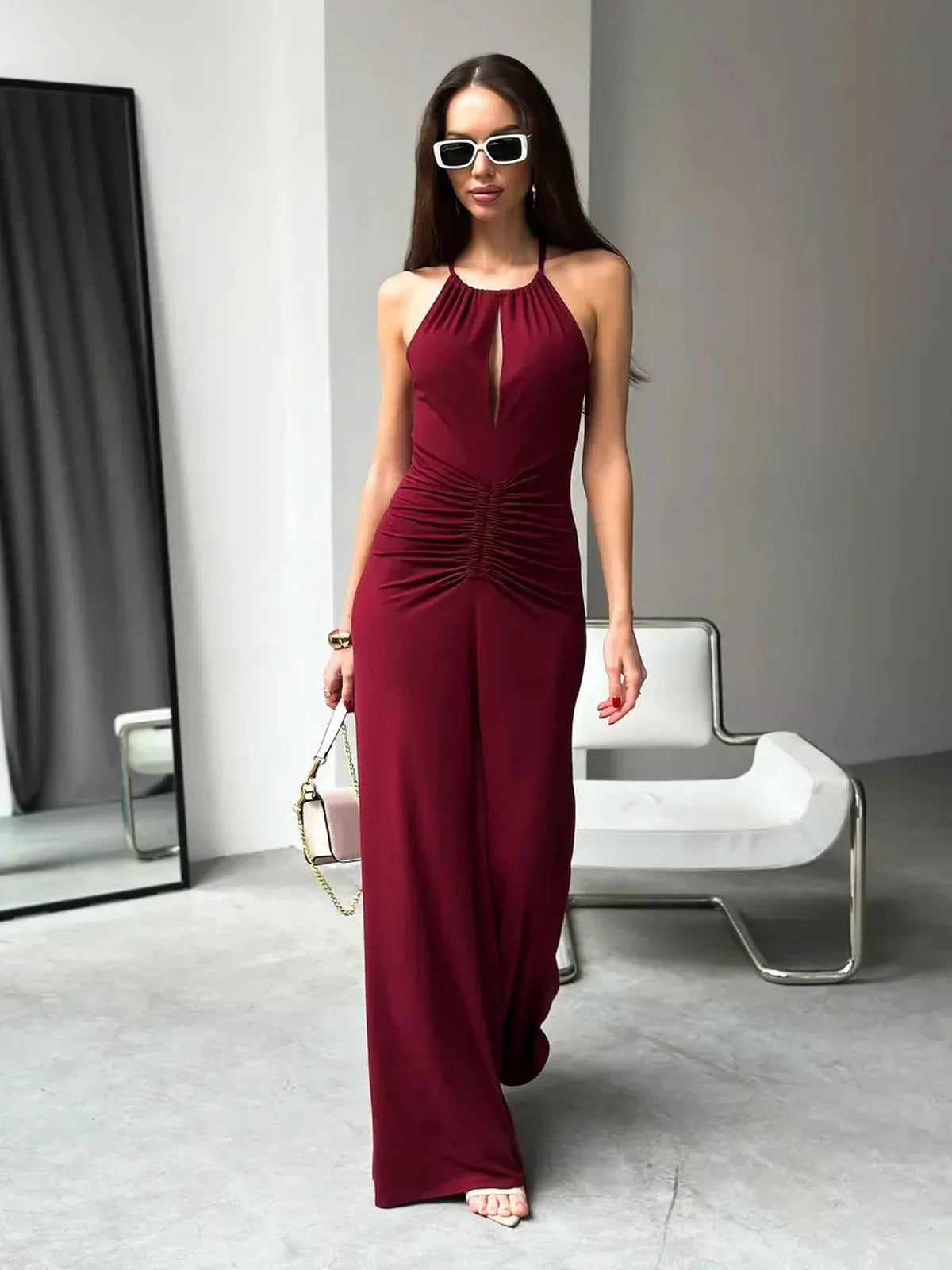 Woman wearing a burgundy maxi dress with a halter neckline and ruched waist, exuding elegance in a modern setting.