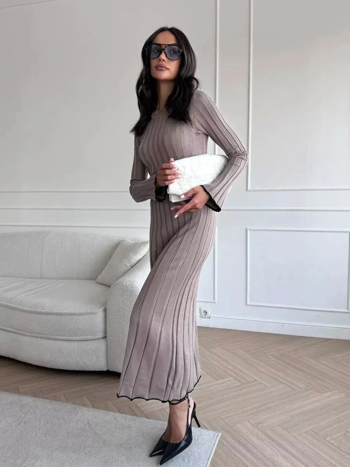 Model wearing a ribbed knit Contour Maxi Dress with long sleeves, black heels, and stylish sunglasses in a modern room.