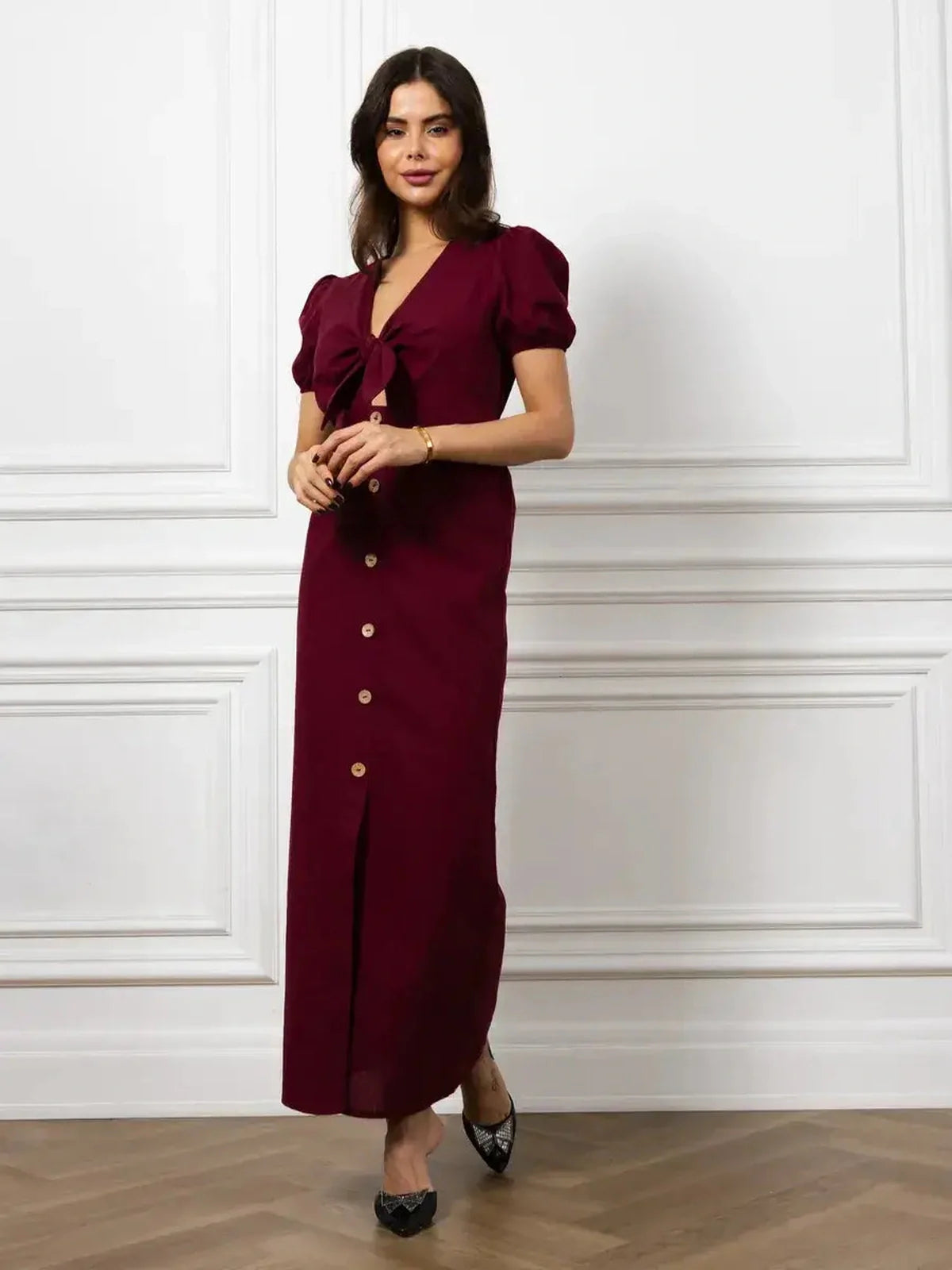 Elegant maxi dress in burgundy with front bow, buttons, and puff sleeves, perfect for a sophisticated look.