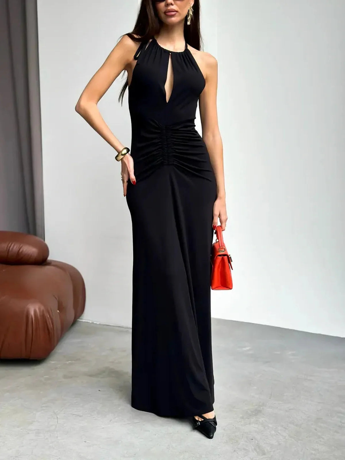 Elegant woman wearing a black Maxi Dress Obsidian with halter neckline and ruched design, paired with a stylish red handbag.