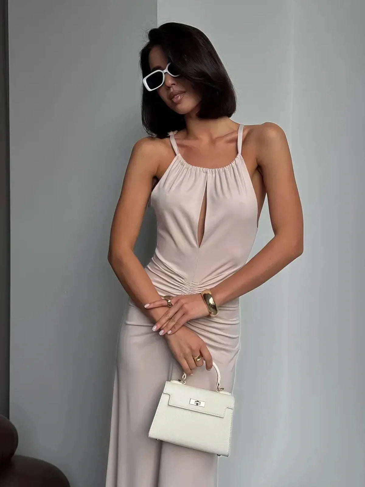 Model showcasing the Serene Curve Maxi Dress with halter neckline and ruched detailing, paired with a white handbag.