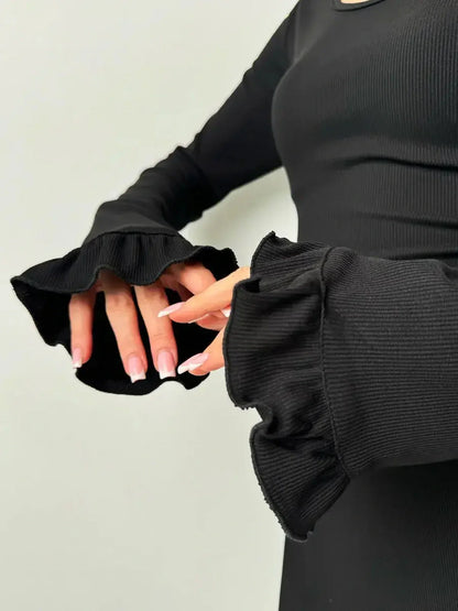 Close-up of model's hands in ruffled sleeves of a black Velvet Lace Mini dress showcasing the textured fabric.