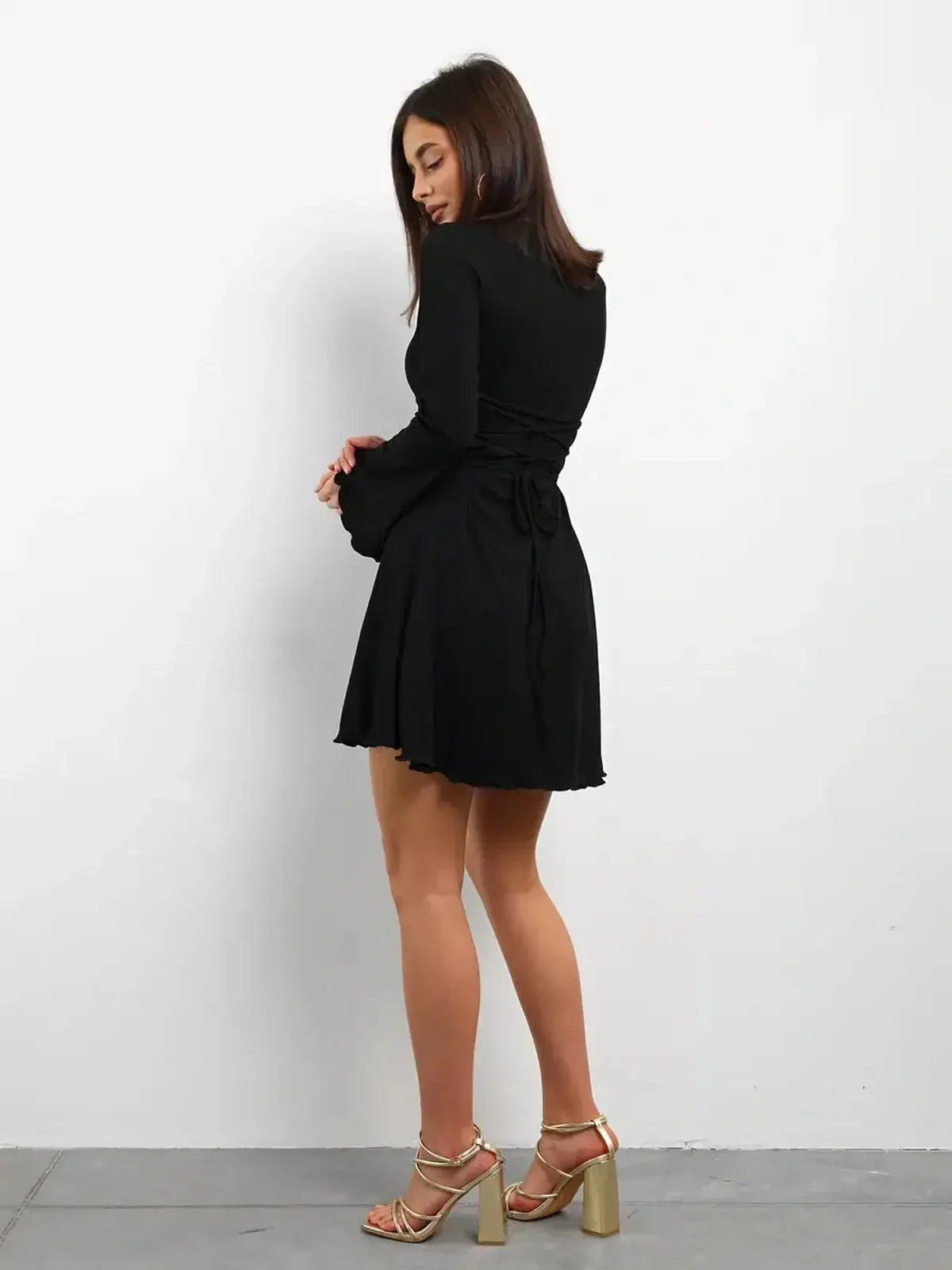 Back view of a woman in a black mini dress with flared sleeves and lace-up detail, perfect for summer or formal events.