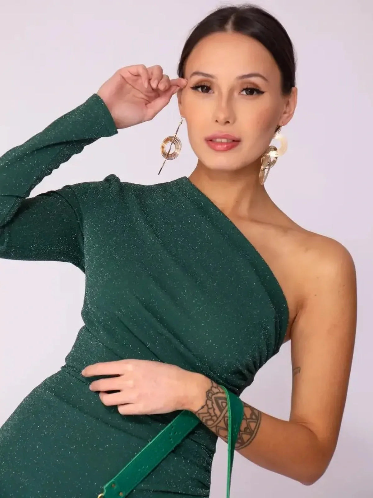 Emerald Spark Maxi Dress showcasing a one-shoulder design and shimmer, highlighted by elegant accessories against a light backdrop.