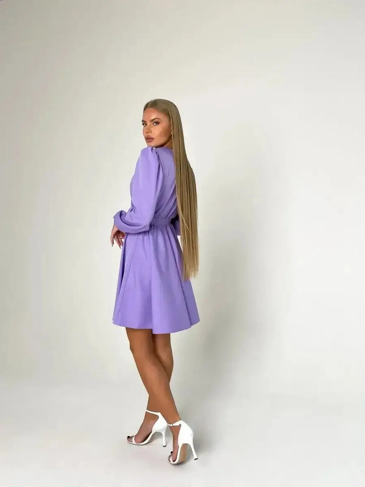 Elegant woman in a lilac mini dress with long sleeves, showcasing a cinched waist and stylish heels.