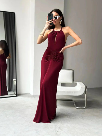 Model in a burgundy maxi dress with draped halter design and ruched waist, showcasing elegance and style.