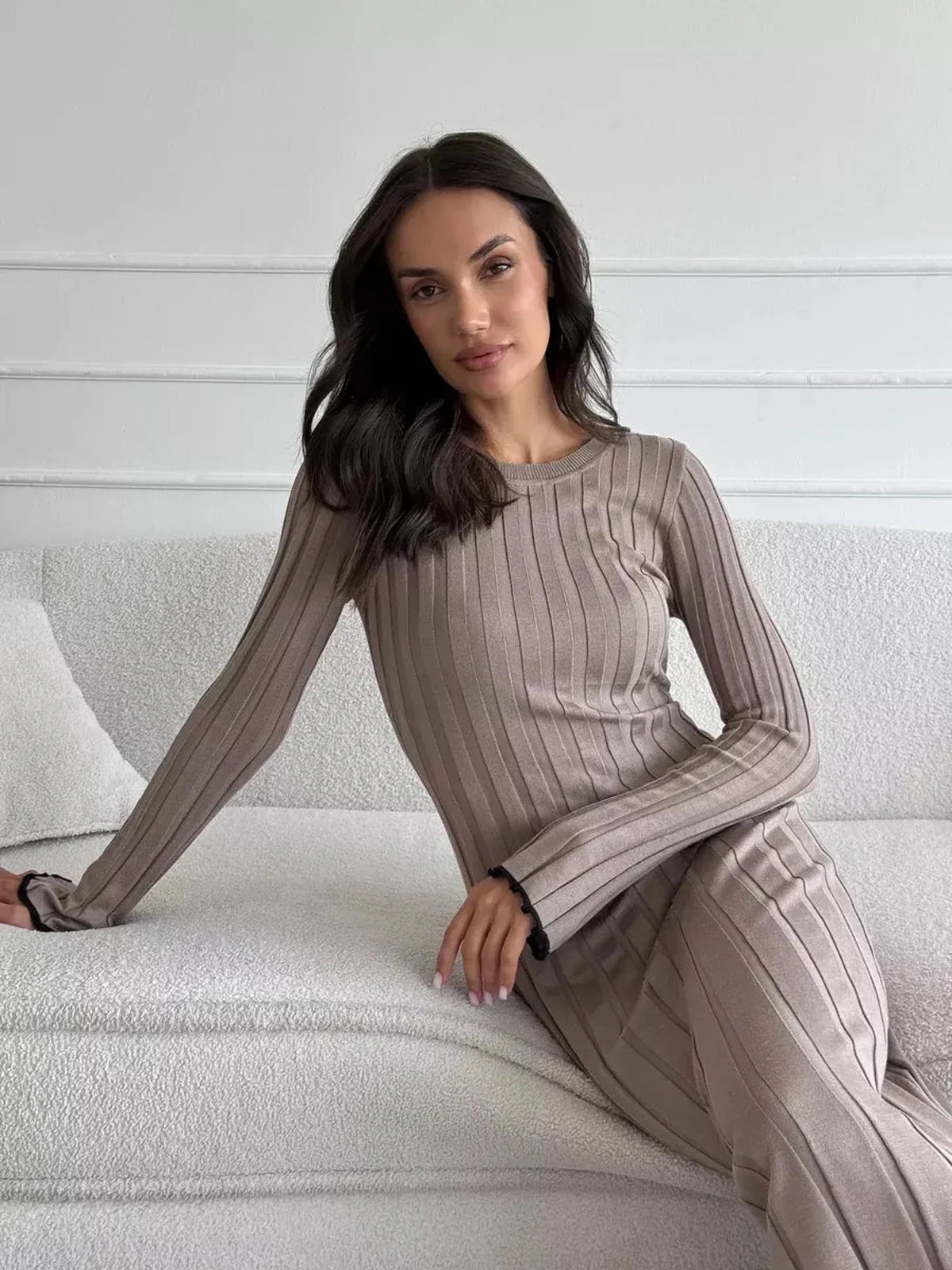 Woman in ribbed knit Contour Maxi Dress, showcasing elegant vertical lines and long sleeves on a cozy sofa.