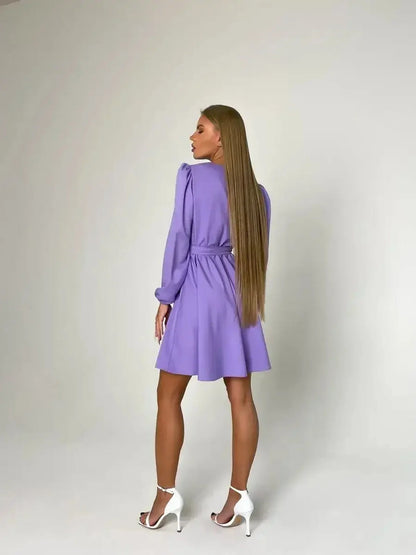 Back view of a woman in a tailored lilac mini dress with long sleeves and a cinched waist, exuding elegance.