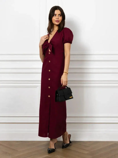 Maxi Dress Merlot Grace with front bow and button detail in rich burgundy, featuring puff sleeves and a deep V-neckline.