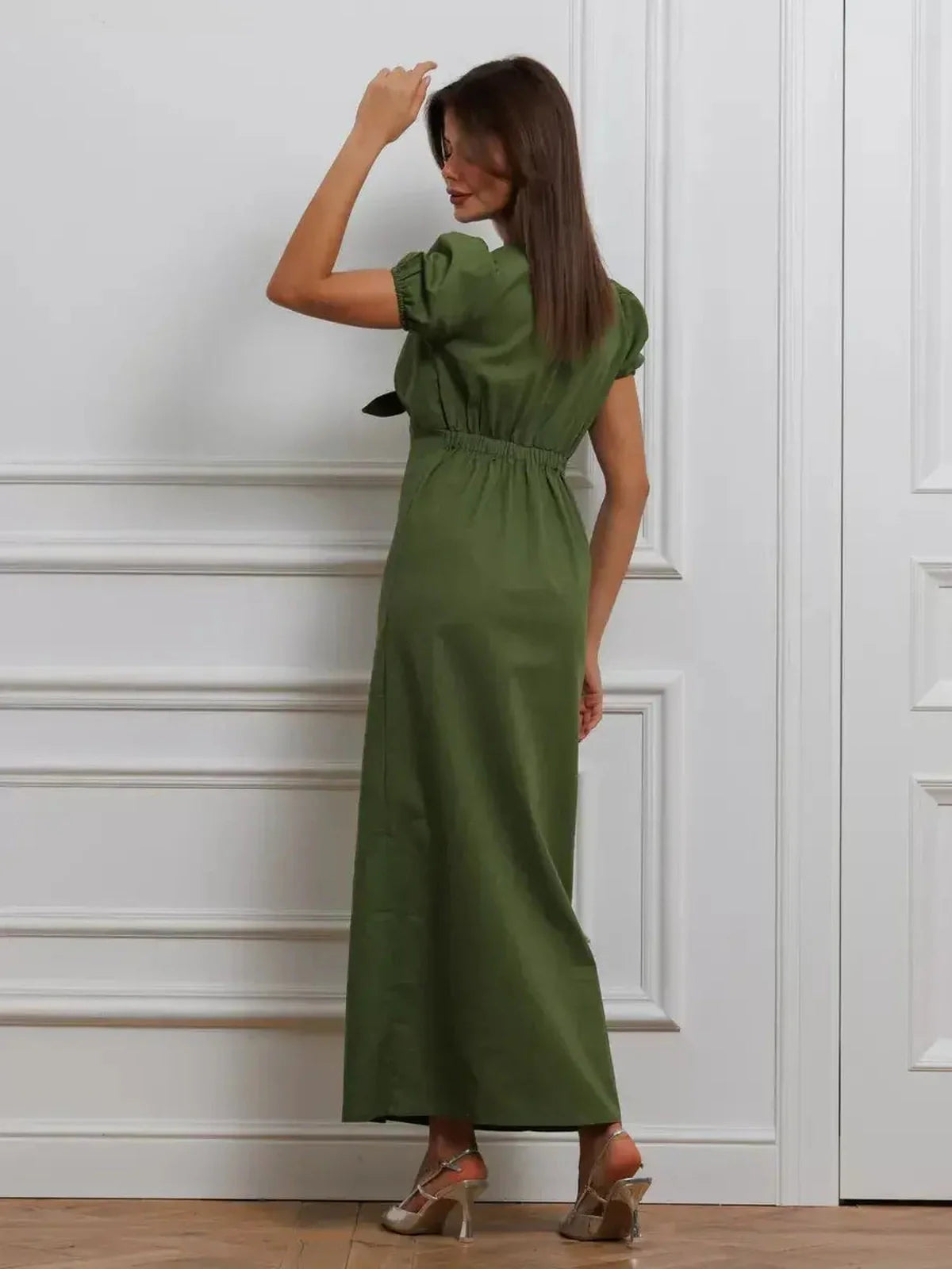 Back view of a woman in an olive green maxi dress with puff sleeves and a tie front detail.