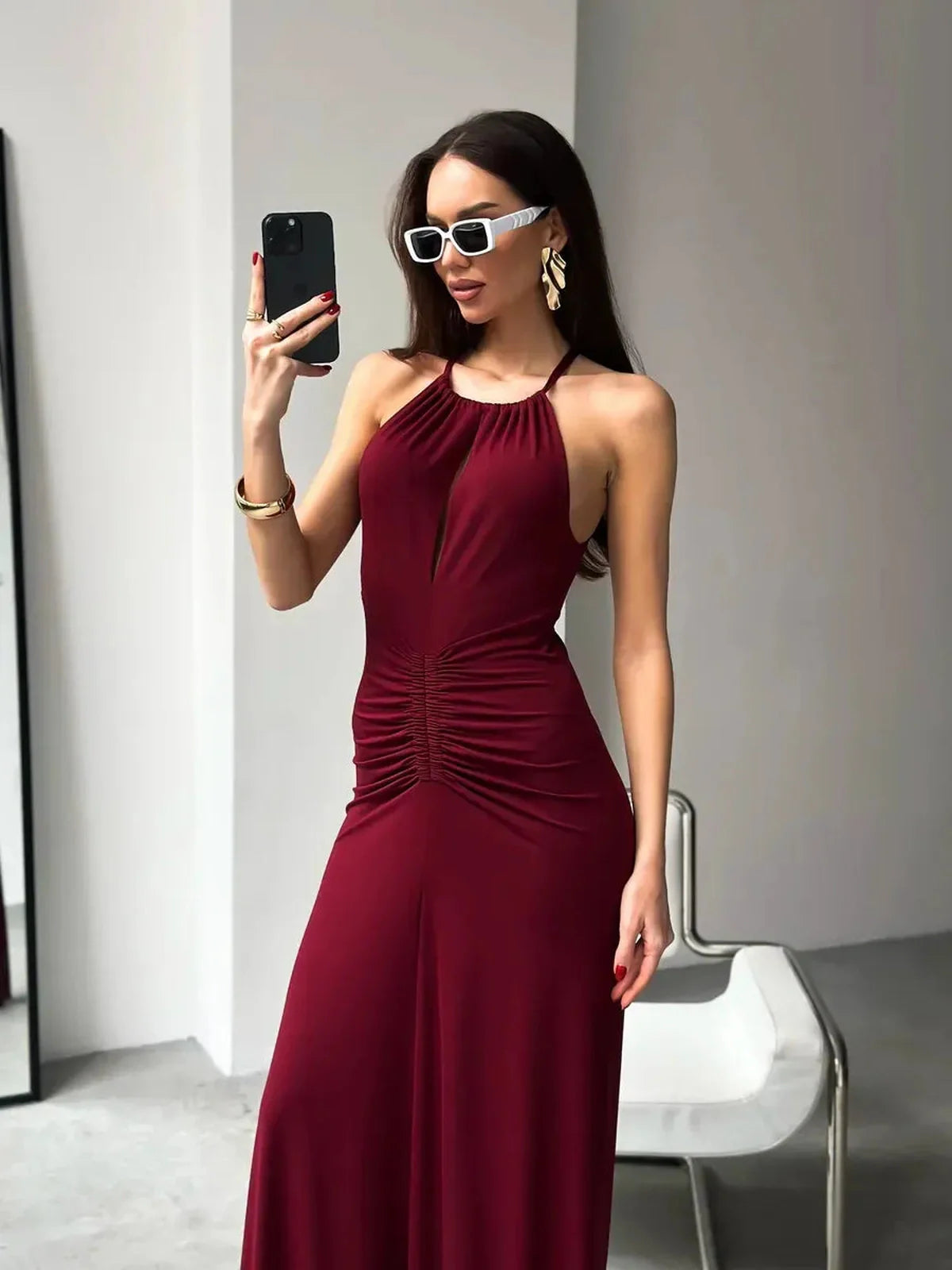 Model in a burgundy maxi dress with draped halter neckline and ruching, showcasing elegance and style.