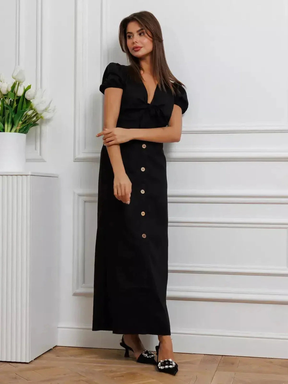 Elegant black maxi dress with tie-front detail, V-neckline, puff sleeves, and contrast buttons.