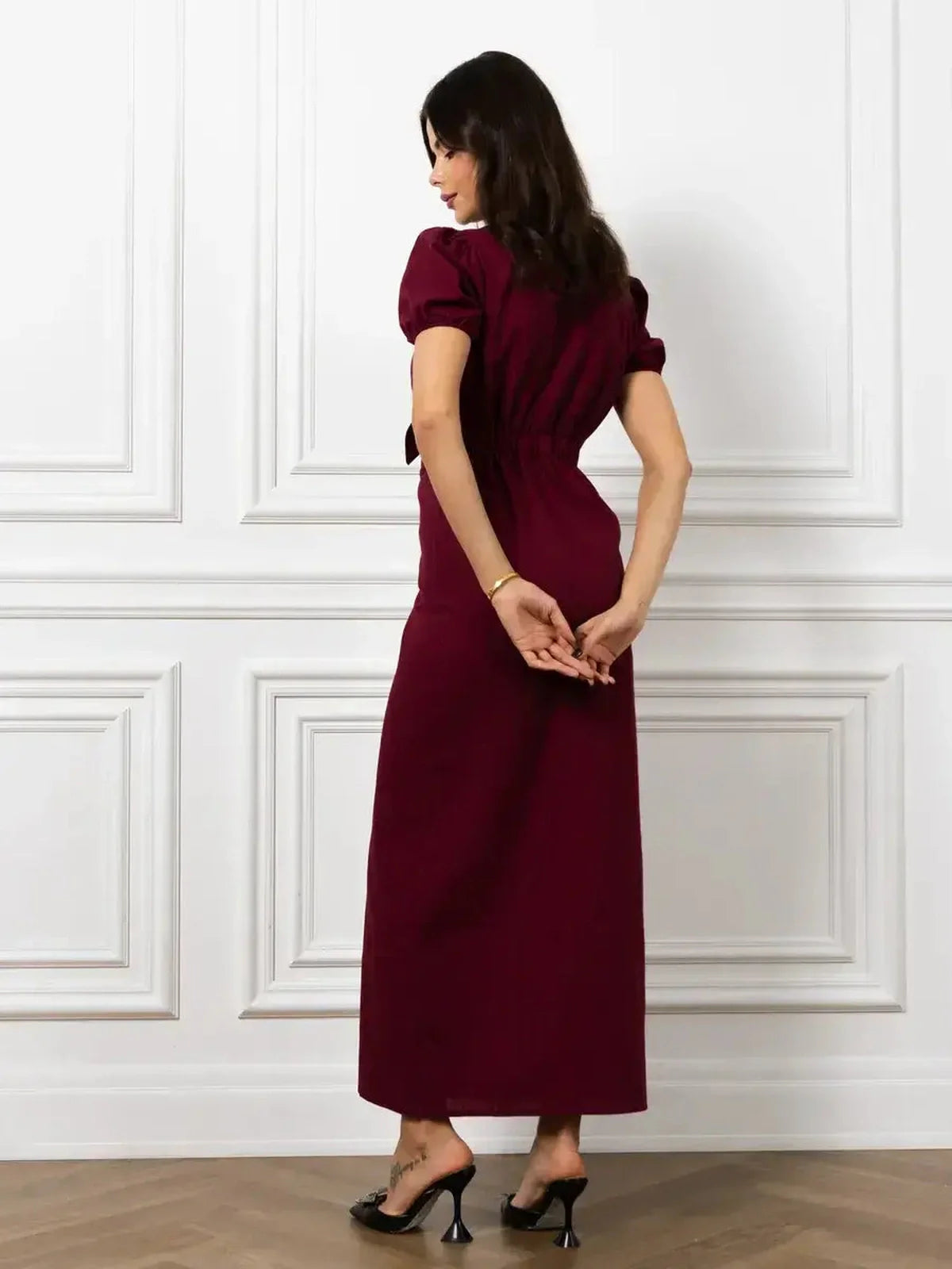 Model wearing the Maxi Dress Merlot Grace, showcasing the back design with puff sleeves and a deep burgundy color.