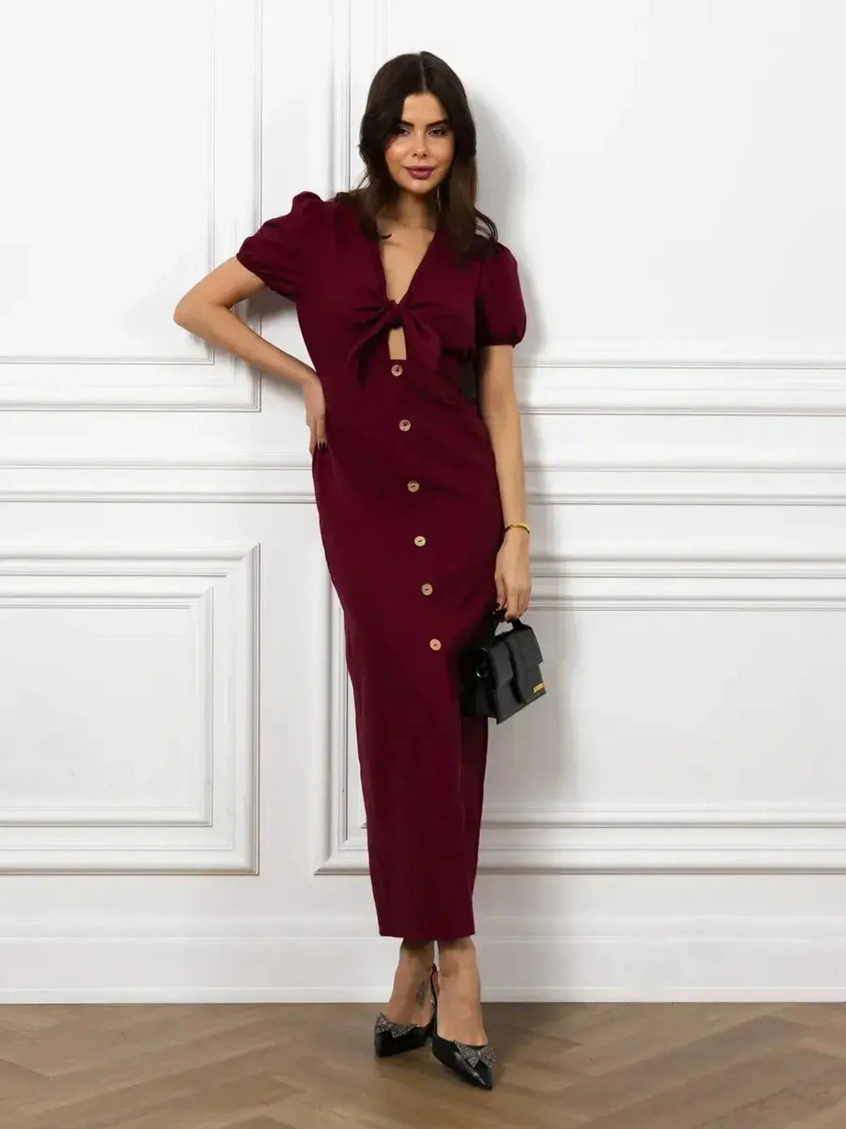 Elegant woman in a burgundy maxi dress with front bow and button detail, showcasing a slim silhouette and puff sleeves.