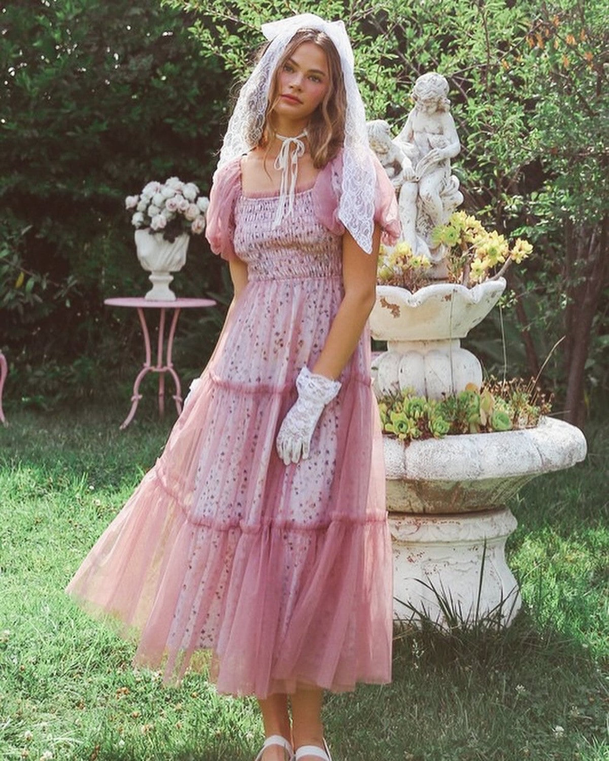 Model wearing a pink floral maxi dress with tulle overlay in a garden setting.