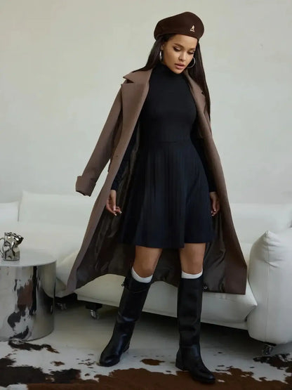 Model in a black ribbed mini dress with a high collar, paired with tall boots and a stylish coat.