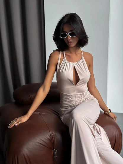 Model wearing Serene Curve Maxi Dress with elegant halter neckline and ruched detailing, seated on a brown couch.