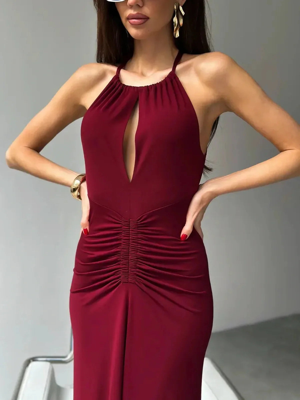 Model wearing the Maxi Dress Élan in burgundy with a halter neck and front keyhole, accentuating a ruched waist.