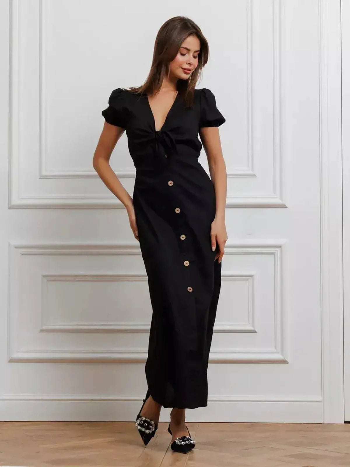 Elegant black maxi dress with tie-front detail, V-neckline, puff sleeves, and contrast buttons for a refined look.