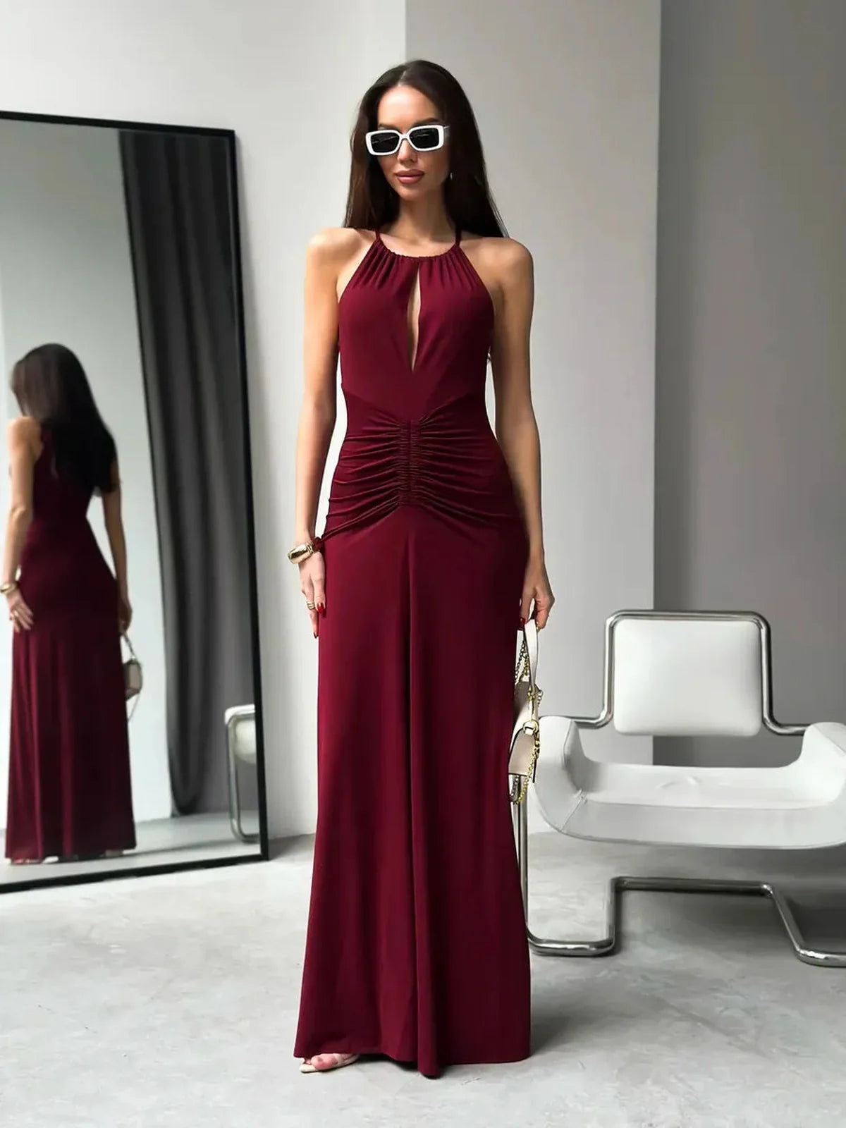 Elegant woman in burgundy halter maxi dress with ruched waist and front keyhole, styled with sunglasses.