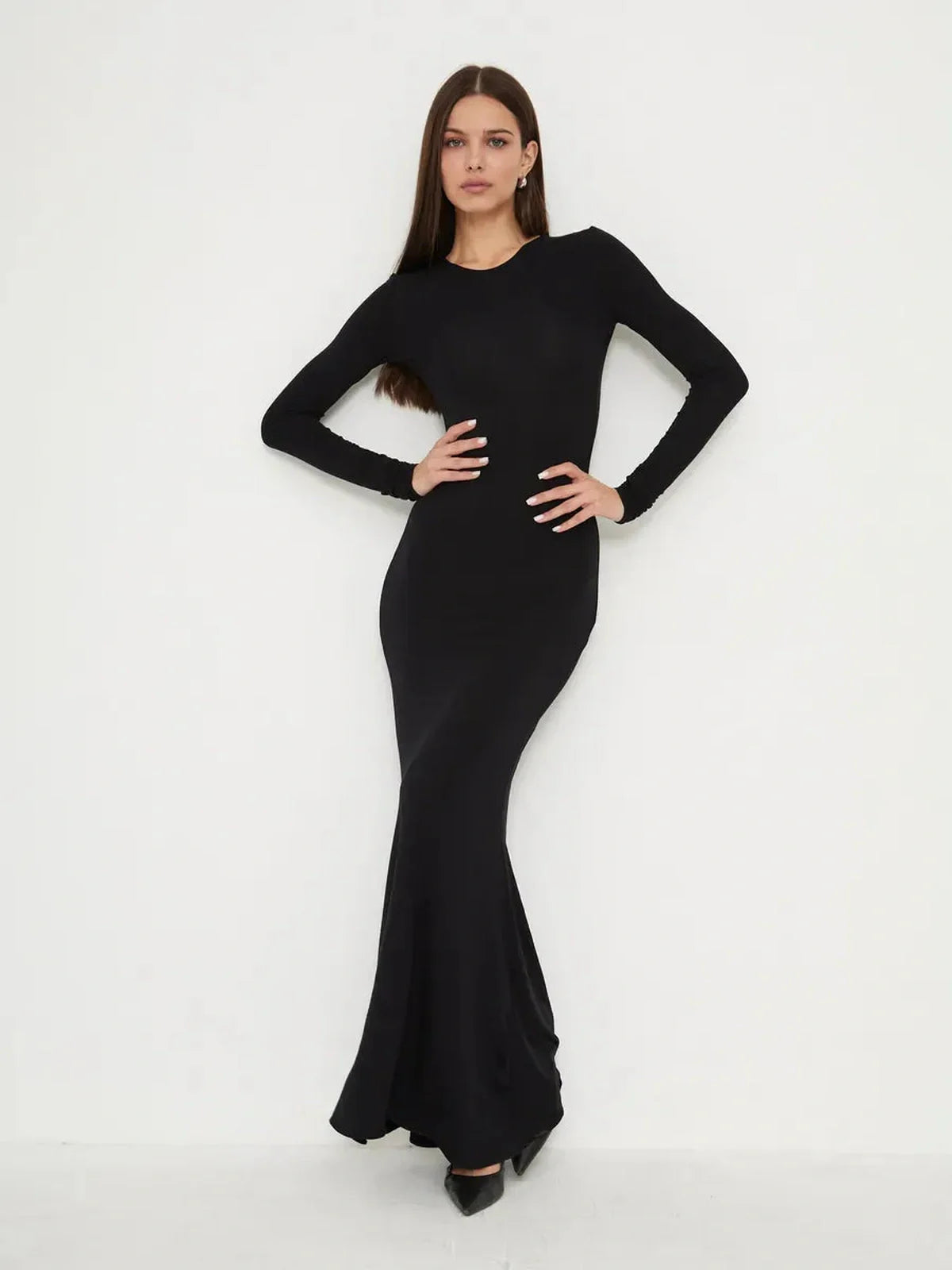 Elegant woman in a full-length black dress with a mermaid hem and long sleeves, showcasing minimalistic style.