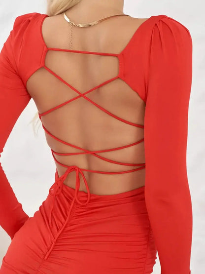 Back view of a long sleeve crimson dress featuring a stylish laced-up design and ruching detail.