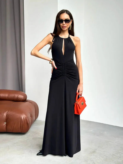 Maxi Dress Obsidian in black with halter neckline, ruched design, and front slit, styled with red handbag and sunglasses.