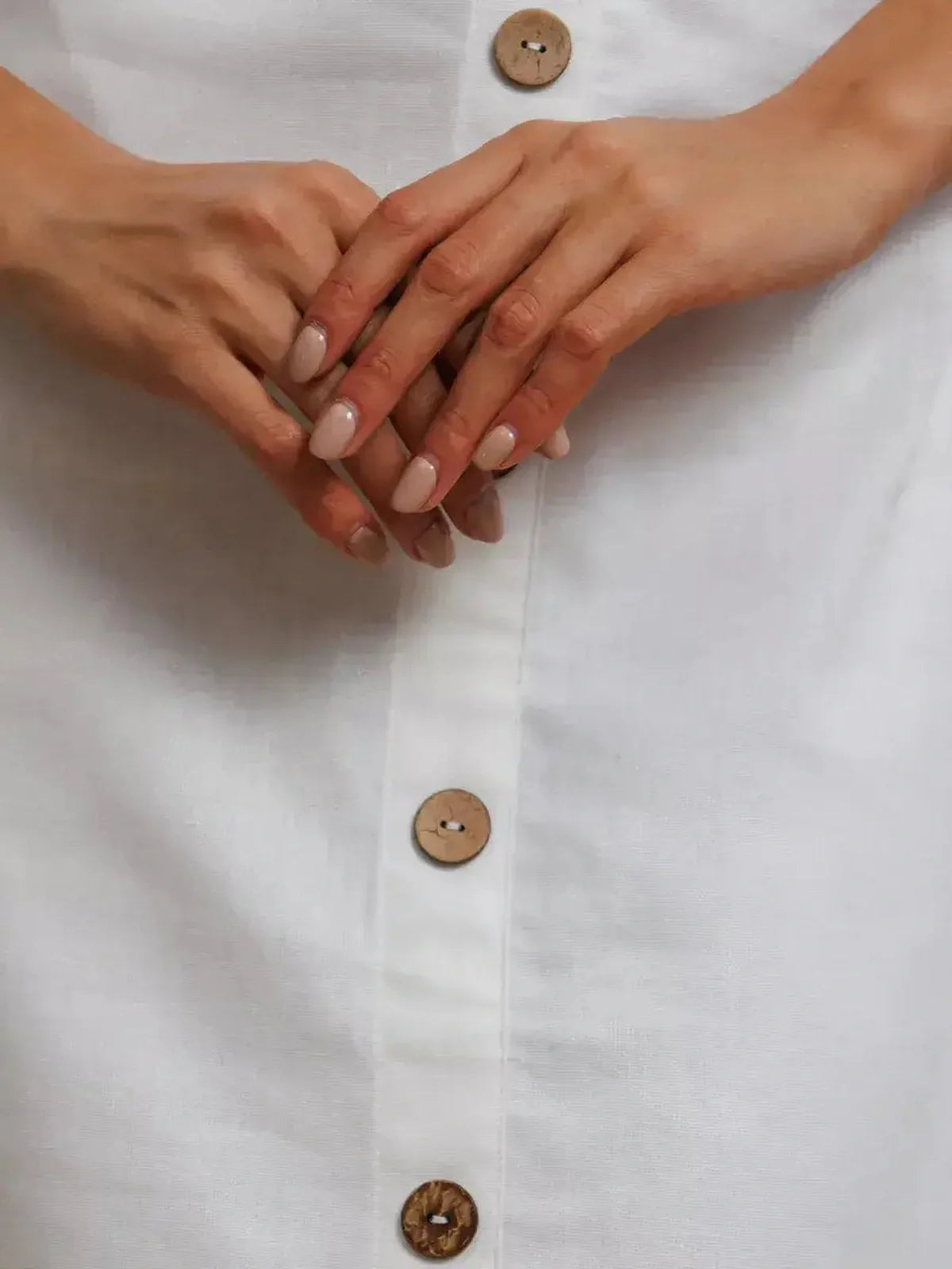 Close-up of hands holding the button-down front of a white maxi dress with natural wooden buttons.