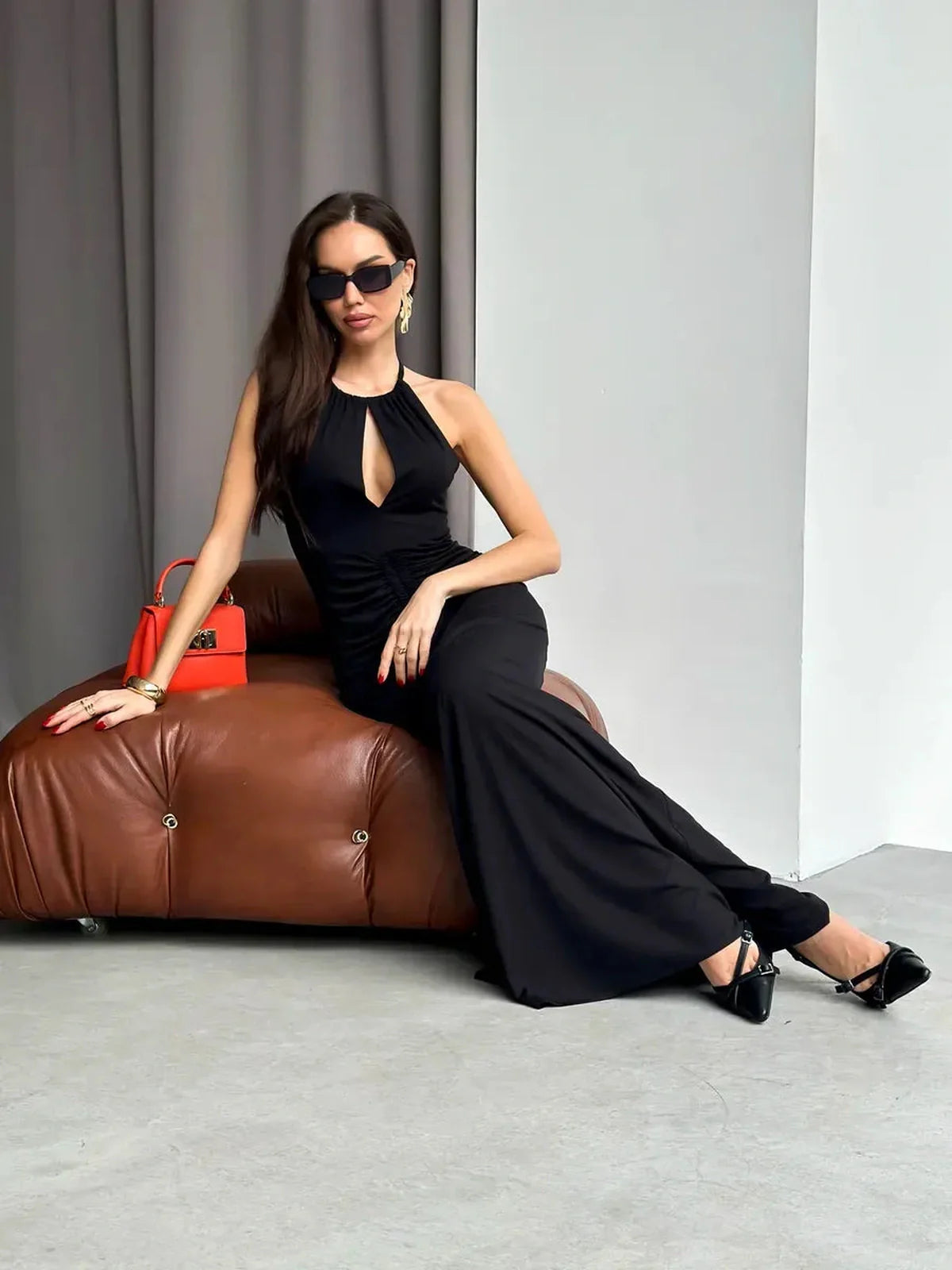 Elegant woman in a black halter maxi dress with keyhole detail, seated on brown furniture.