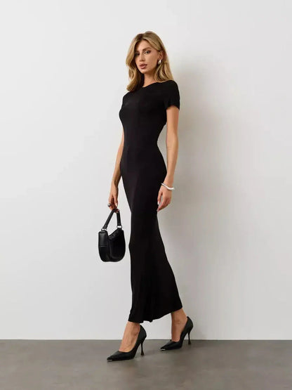 Model wearing the Noir Curve Maxi Dress, a sleek black dress with a sculpted silhouette and flared hem, styled with heels.