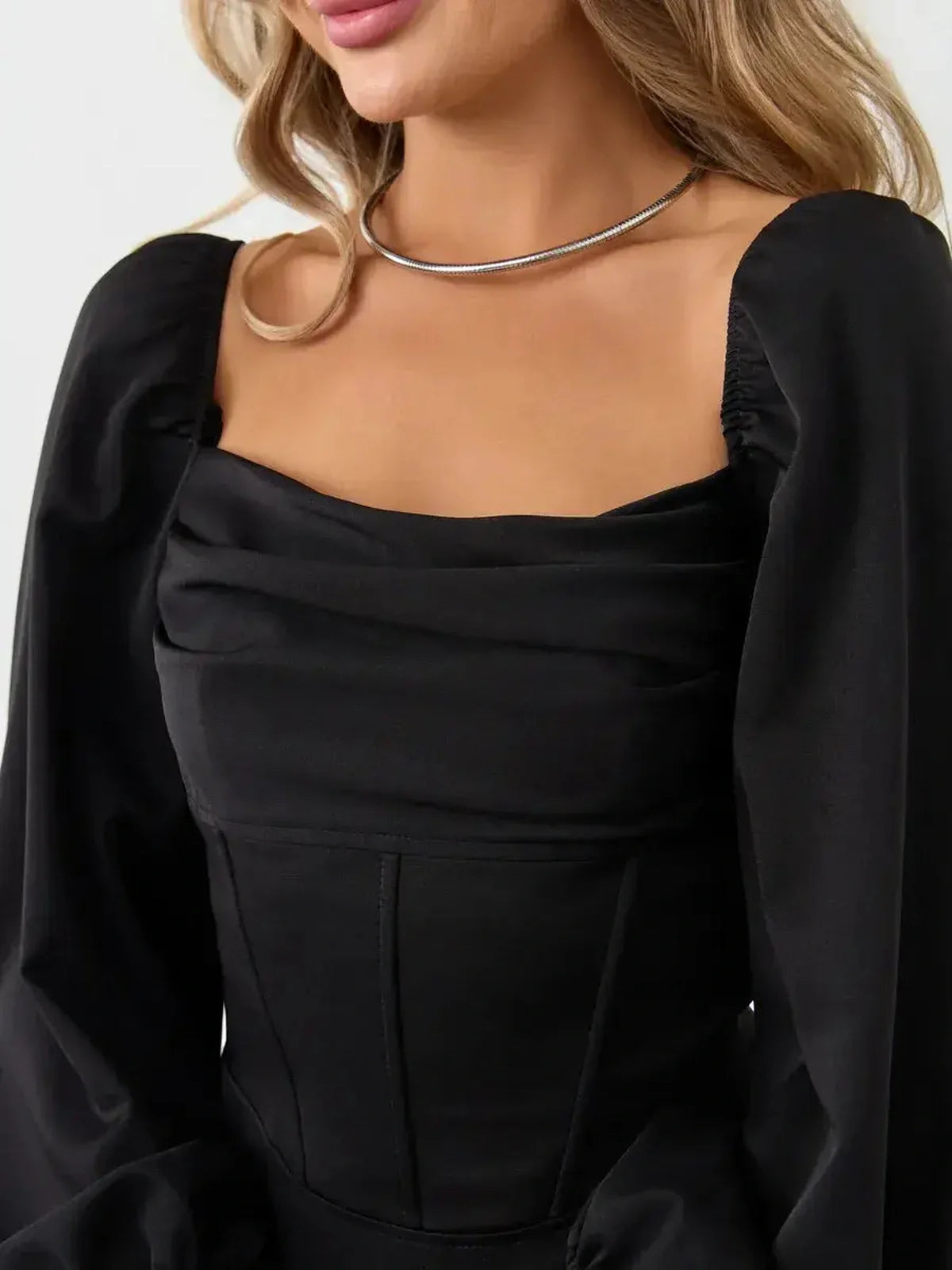 Close-up of a woman in a black velvet corset dress featuring a structured square neckline and voluminous sleeves.