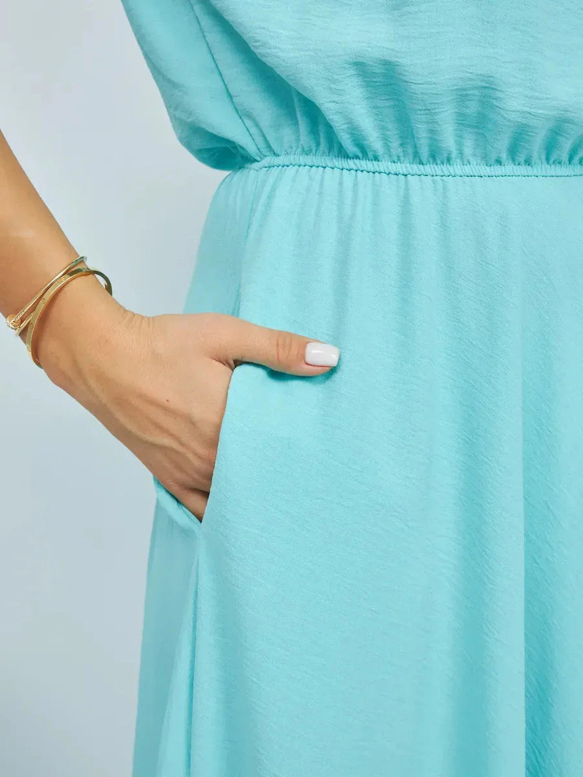 Close-up of a hand in the pocket of a light blue dress, showcasing the fluid fabric and effortless style.