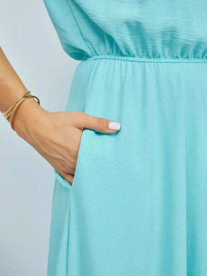 Close-up of a hand in the pocket of a light blue dress, showcasing the fluid fabric and effortless style.