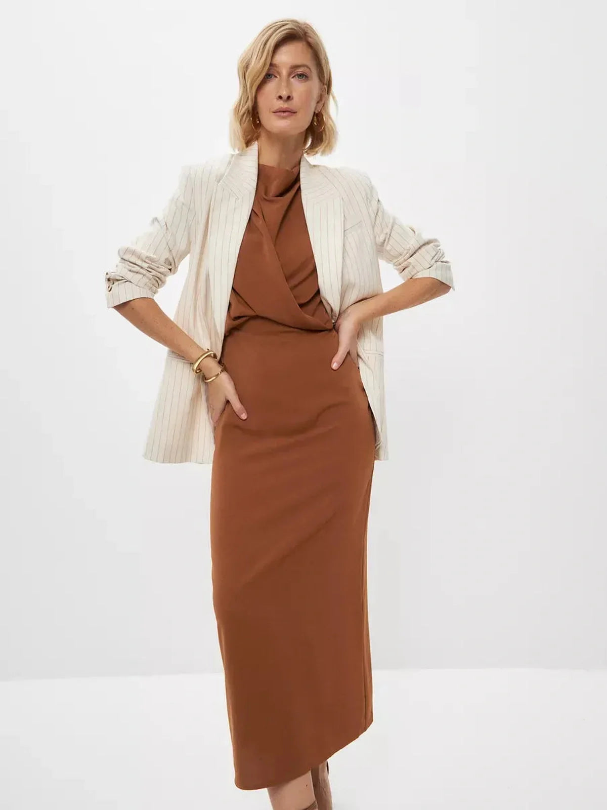 Model showcasing a Sculpted Drape Maxi Dress in warm brown, styled with a chic blazer for elegant evening attire.
