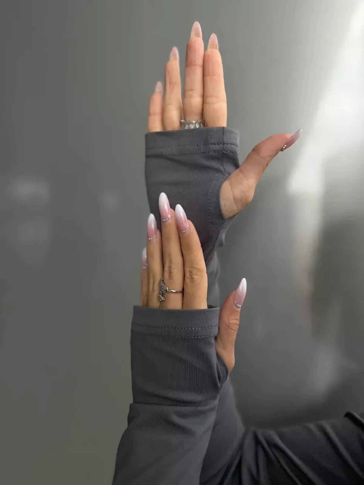 Close-up of hands wearing gray long sleeve dress with unique fingerless design, showcasing stylish nails.