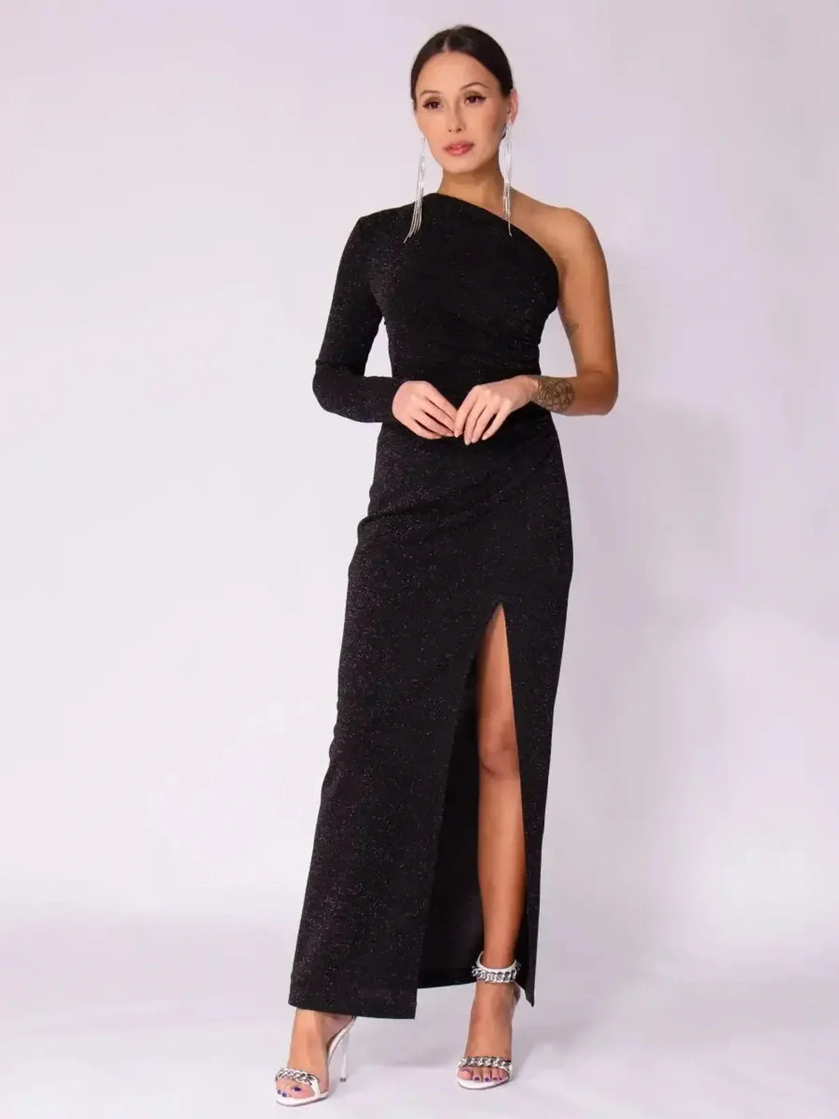 Woman in a black Luna Noir Maxi Dress with one-shoulder design and leg slit, exuding elegance and sparkle.