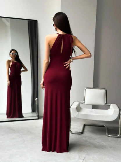 Elegant woman in a burgundy halter maxi dress showcasing a ruched waist and back keyhole detail in a chic indoor setting.
