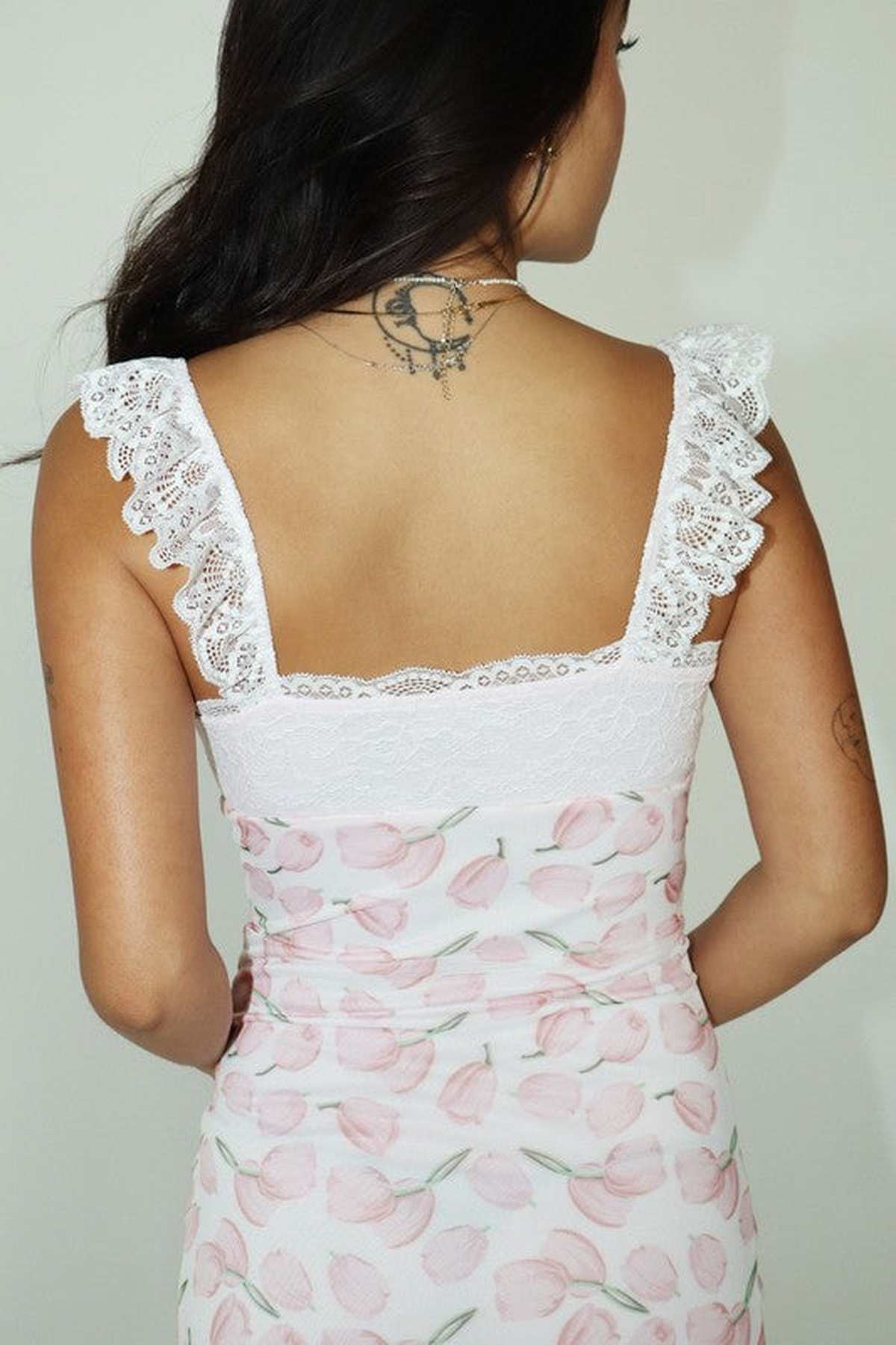 Back view of a woman wearing a floral dress with lace straps, showcasing a stylish pink tulip pattern.