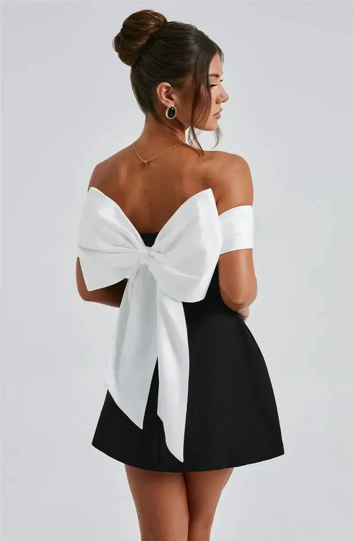 Model showcasing the Alba Mini Dress, featuring an oversized white bow and off-shoulder satin neckline for a chic look.