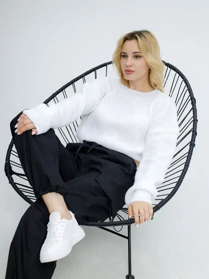 Woman wearing Alba Pullover by Lauven, a lightweight knit in soft white, seated casually in a modern chair.