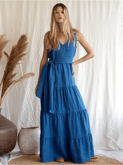 Model wearing the Azure Grace Maxi Dress in deep blue linen, showcasing its flowing tiered silhouette and open back design.