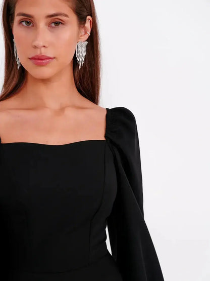 Model wearing a black mini dress with puff sleeves and square neckline, showcasing a chic evening look.